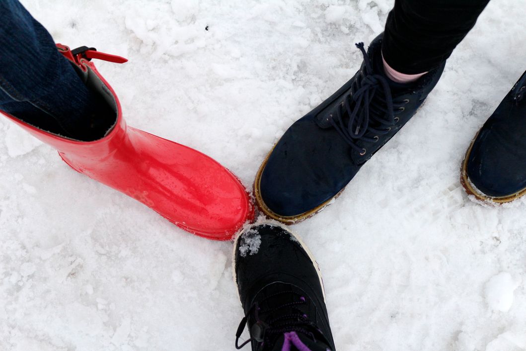 Kolme jalkaa missä kolme kenkää kengä'nkärjet vastakkain lumisessa maassa.