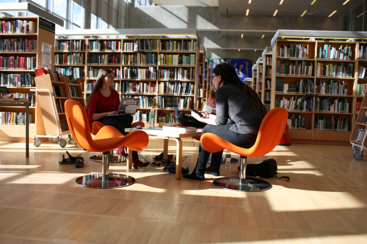 Kolme nuorta istuu kirjastossa pöydän ääressä