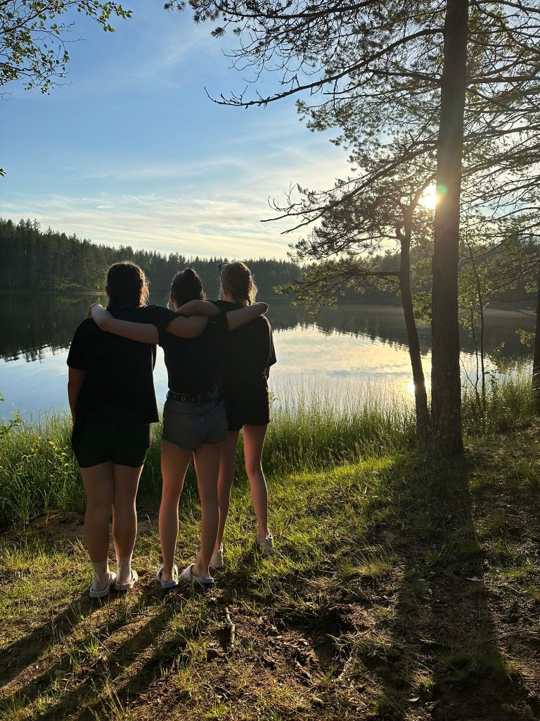 Kolme tyttöä katsovat ilta aurinkoa järven rannalla leirin viimeisenä iltana.