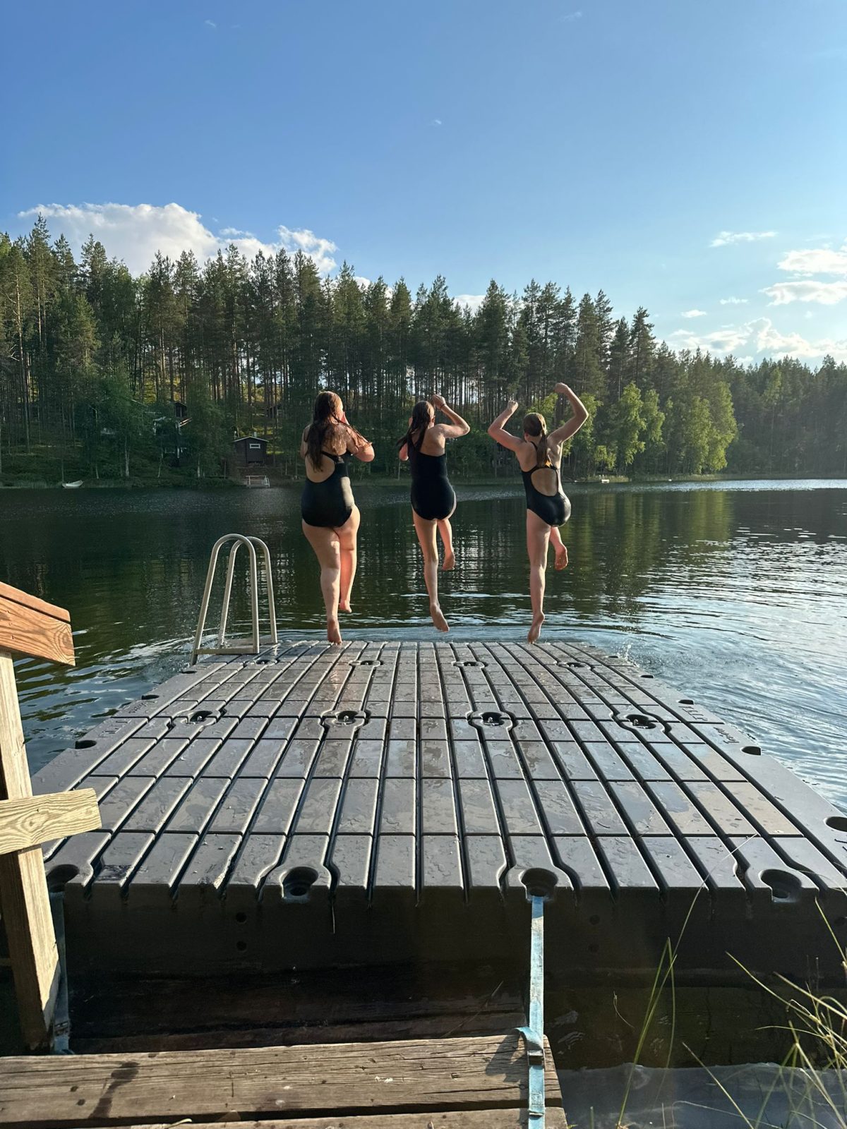 Kolme nuorta hyppäämässä laiturilta järveen.